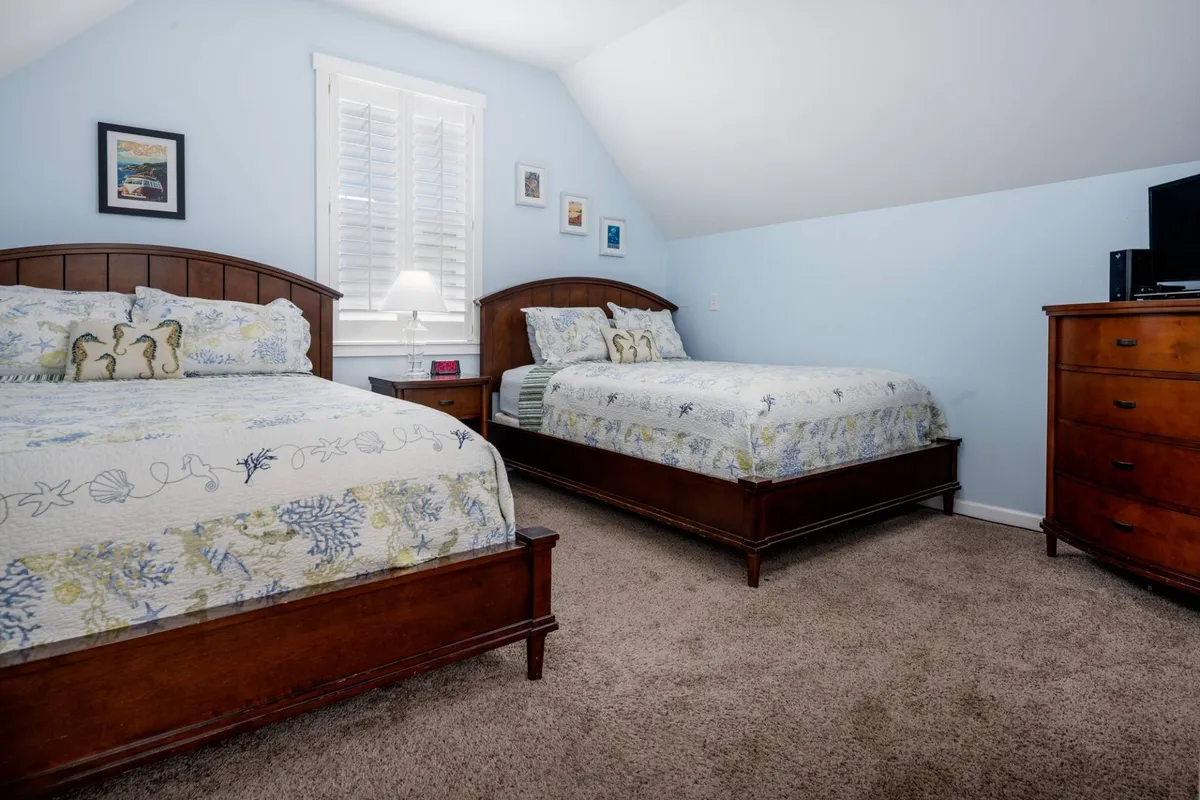 A cozy bedroom scene with two wooden beds adorned with decorative pillows and lamps on a dresser. The warm, intimate layout is perfect for siblings, friends, or children sharing a space.