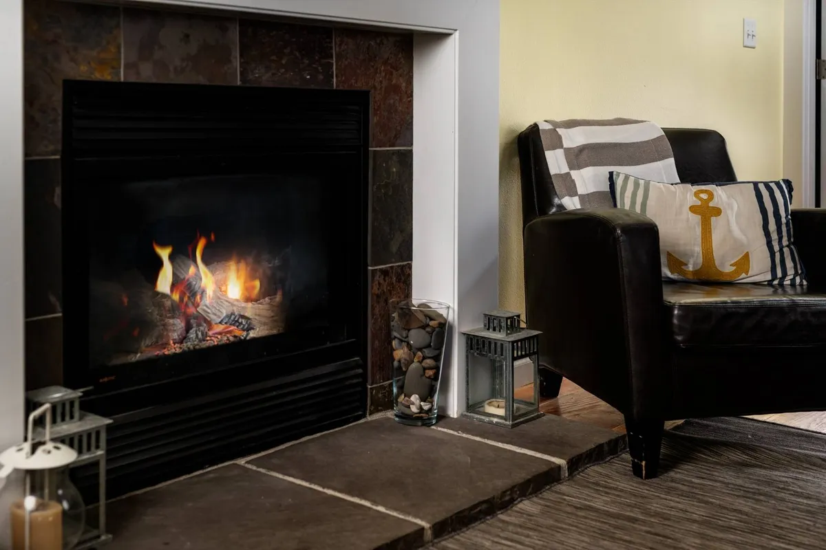 A cozy living room centered around a fireplace, with an inviting armchair, decorative pillows, and lanterns. The space feels warm and perfect for group movie nights or intimate conversations after a long day of exploring the coast.