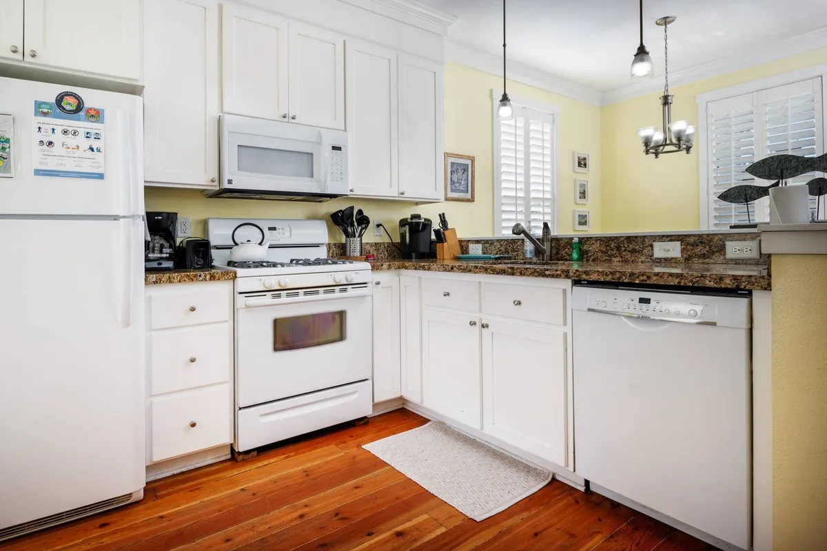 A well-equipped kitchen with white cabinetry, granite countertops, modern appliances, and warm wooden flooring. The space is organized and inviting, perfect for cooking and entertaining family or friends.