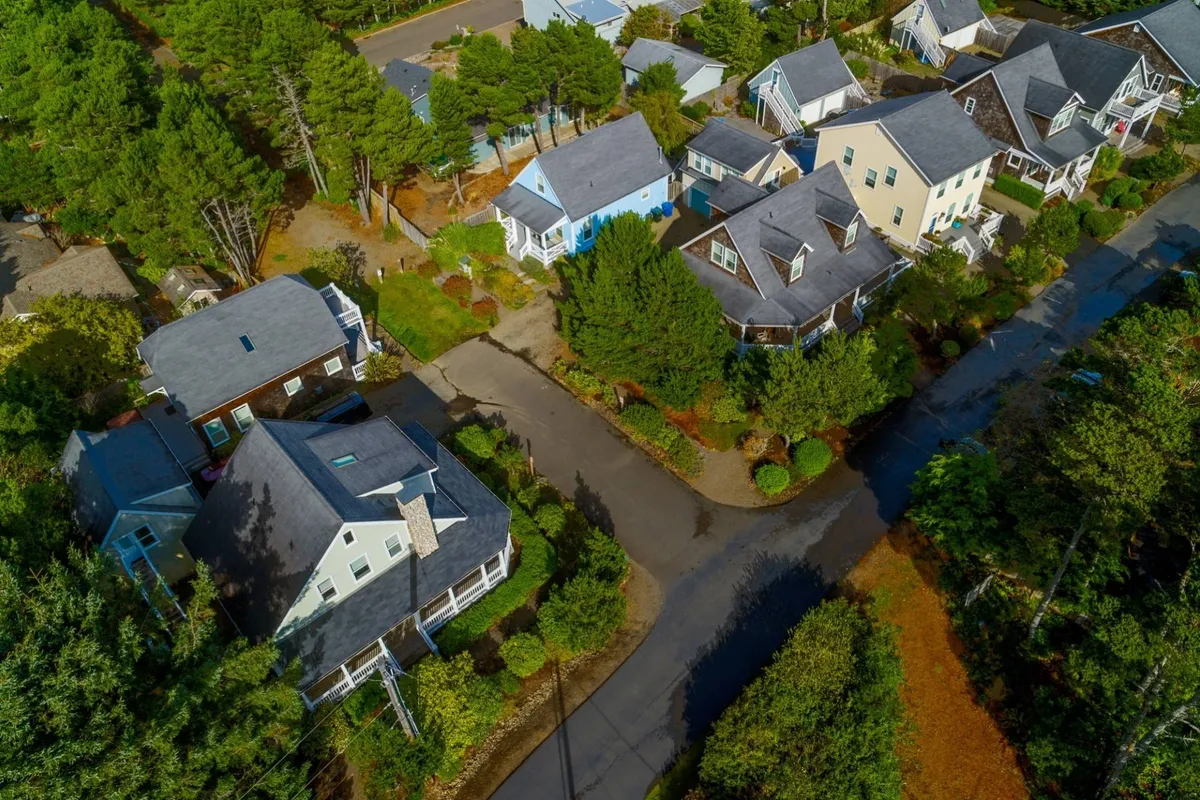 A welcoming exterior view of the neighborhood with neatly arranged houses, tree-lined streets, and well-maintained gardens. People are seen strolling and gathering outdoors, capturing the essence of a friendly and peaceful community.