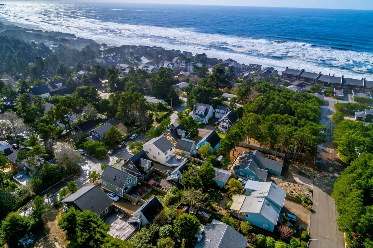 A scenic coastal view featuring ocean waves, lush green trees, and a row of colorful houses. The area feels vibrant yet serene, suggesting proximity to both nature and community life.